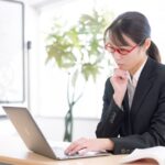 パソコンを使いながら集客方法を考えるスーツ姿の女性