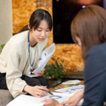 女性が資料を手に持ち、商談相手にグラフを指し示しながら提案している様子