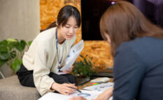 女性が資料を手に持ち、商談相手にグラフを指し示しながら提案している様子