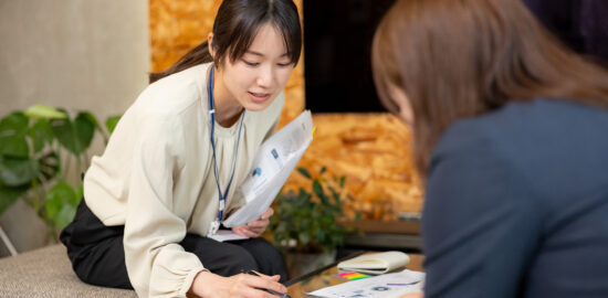 女性が資料を手に持ち、商談相手にグラフを指し示しながら提案している様子
